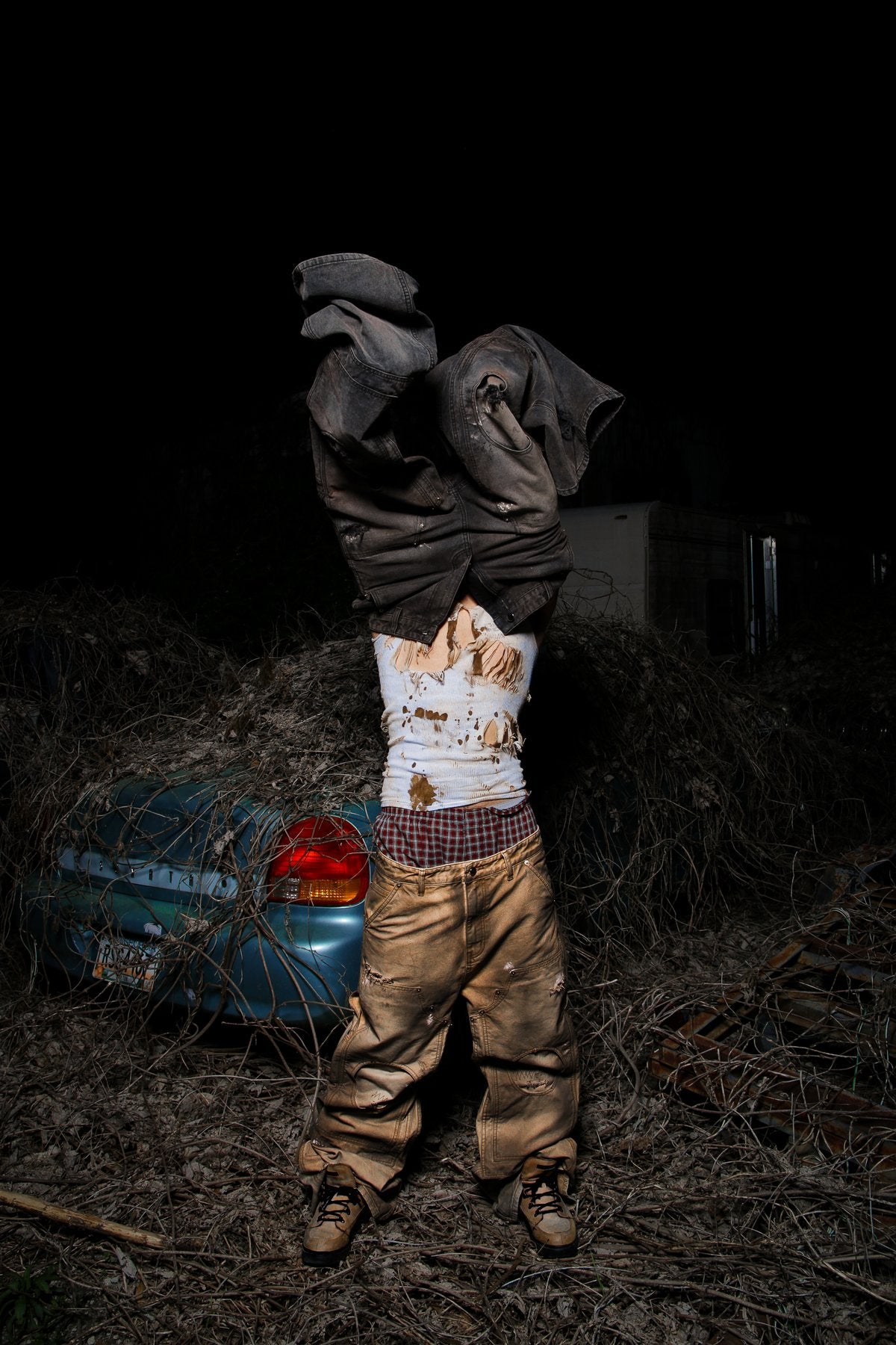 Profit Minded — figure pulling a work jacket overhead beside a wrecked car at night